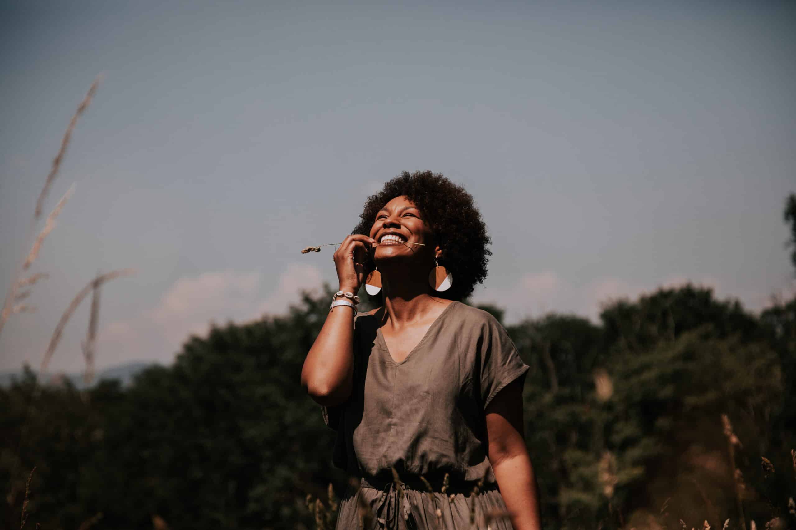 Une jeune femme se tient dans les champs, les cheveux crépus dans le vent. 