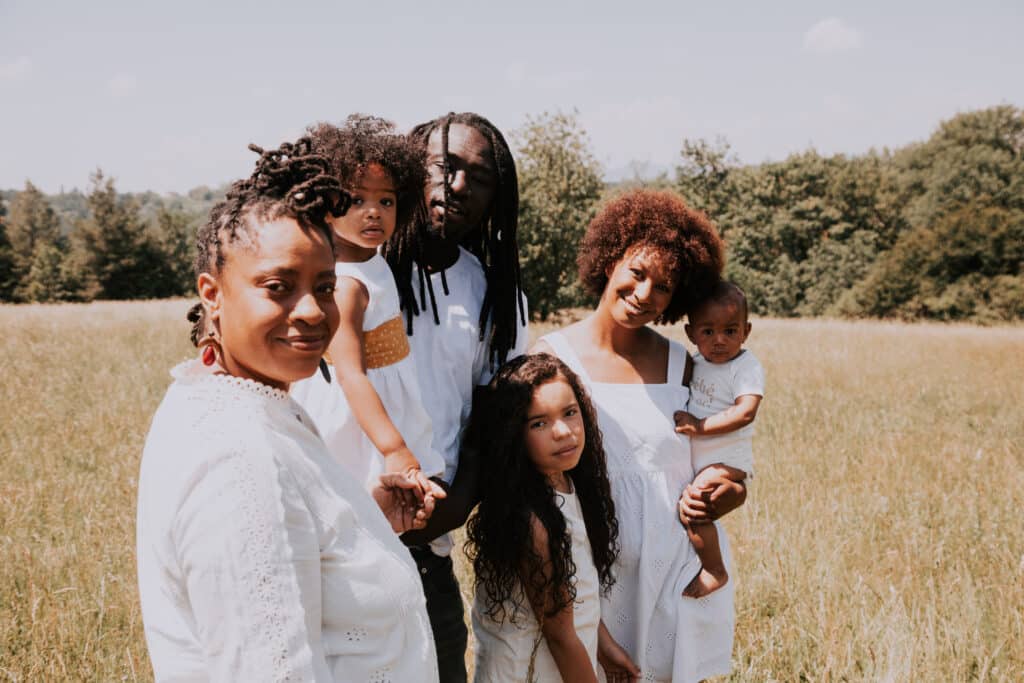 Une famille de personnes noires se tient dans un champ de blé. Les deux parents sont accompagnés de leur quatre enfant qui ont entre 24 et 1 an.