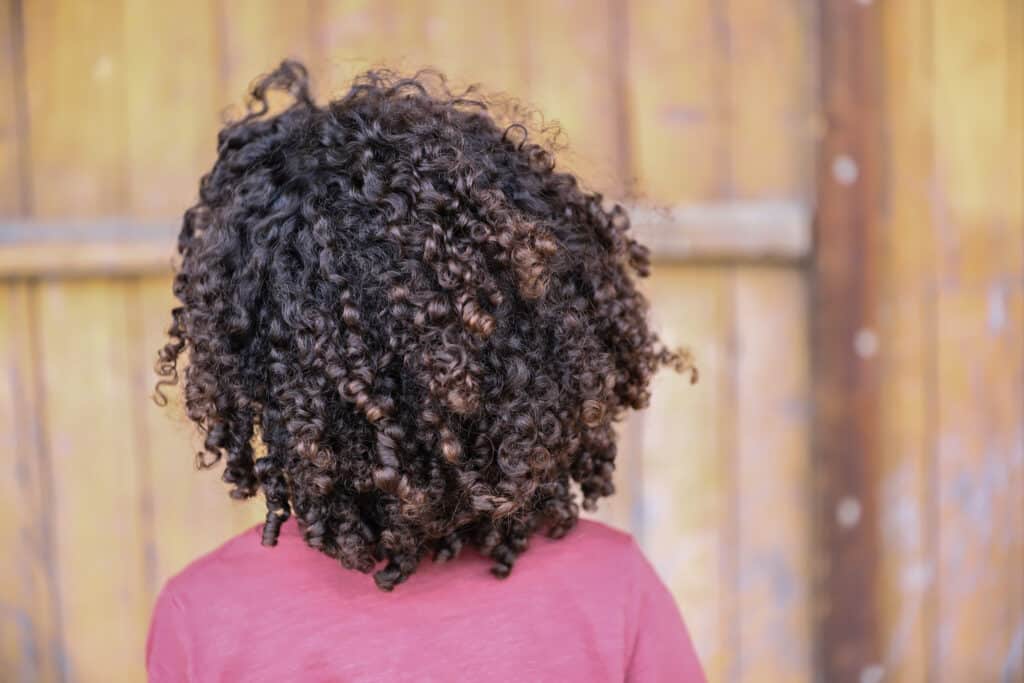 Une personne se tient de dos, avec un tee-shirt rose, on voit ses cheveux frisés.